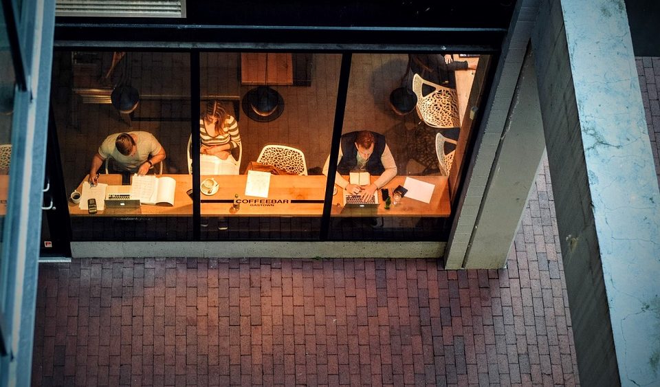 Two men and a woman working near a glass window under dim lighting.