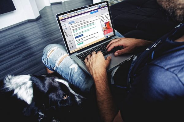 A man uses a laptop with his dog sitting next to him.
