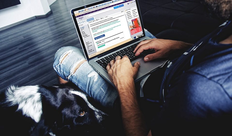 A man uses a laptop with his dog sitting next to him.